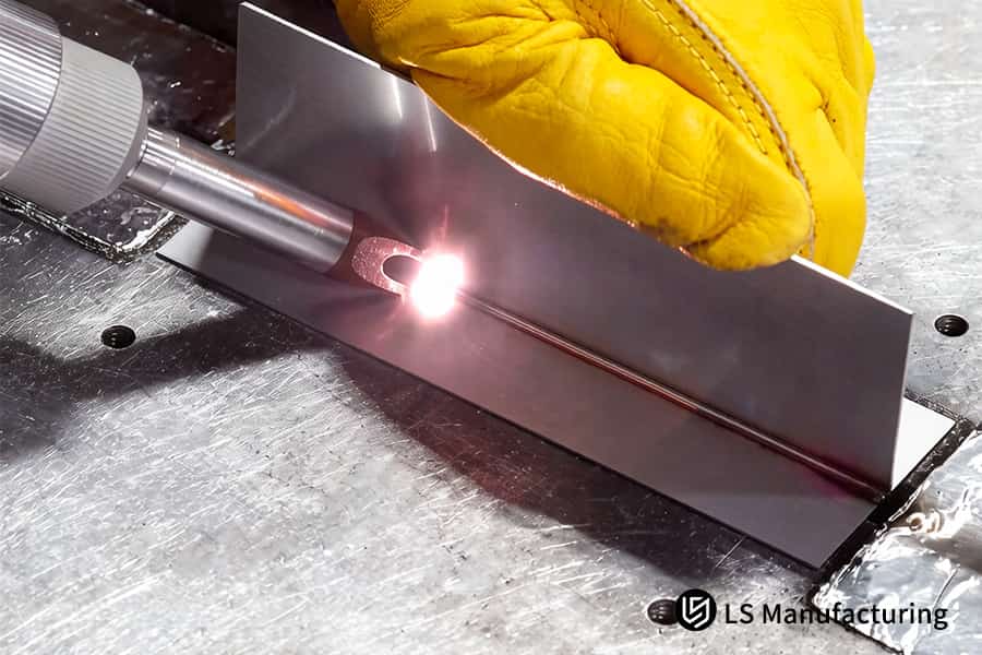 A hand steadies a 304 stainless bracket as a laser spot welds it for medical instrument or probe assembly.